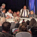 Les dignitaires assis à une table et le public regardent le président de NTI, Aluki Kotierk, signer l’Entente sur le transfert des responsabilités liées aux terres et aux ressources du Nunavut.