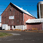Un silo et une grange brune avec un panneau indiquant la ferme Mādahòkì.