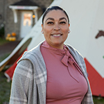 Paulete Poitras, smiling in front of a white tipi decorated with a red pattern and an image of a horse.