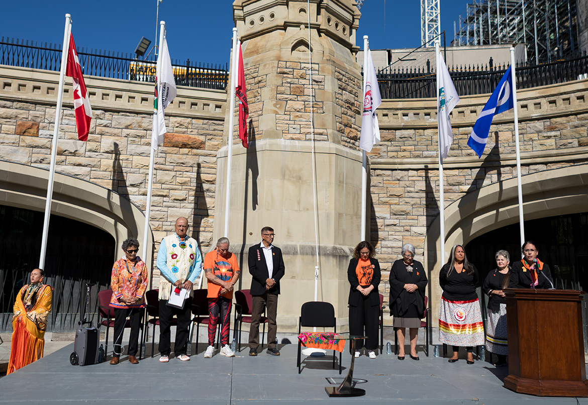 People standing on a stage at Parliament Hill during the 2025 re-raising of the Survivors' Flag ceremony.