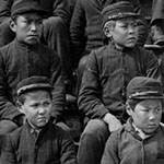 Dix-neuf (19) élèves autochtones assis sur les marches à l'extérieur du pensionnat indien Metlakatla, en Colombie-Britannique.