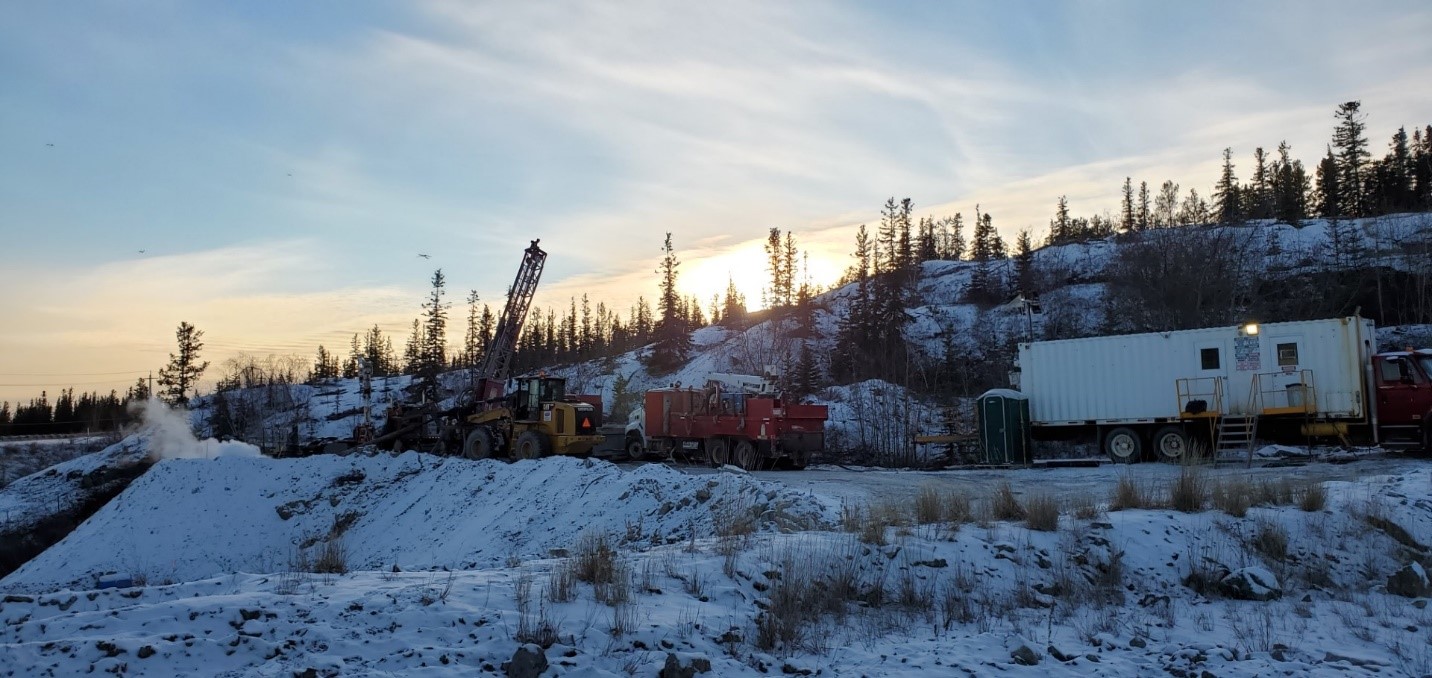 Drilling equipment and machinery working on site on the underground stabilization work. The landscape is covered in snow, and the sun is backlighting the trees in the background